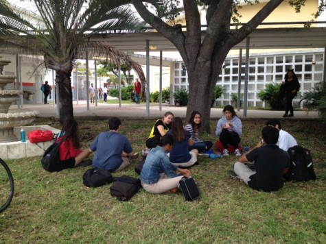 Students gather in the shade in front of the auditorium. 