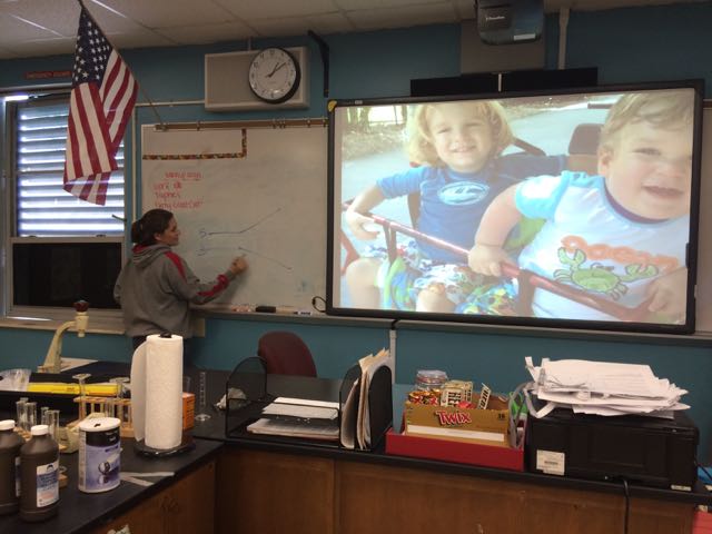 De La Vega teaches her students about DNA replication. Her two sons are larger-than-life as her screensaver.