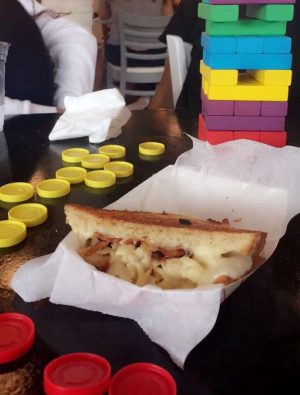 The "Mackin Melt", a grilled cheese with creamy mac-n-cheese and crispy bacon, next to some board games.