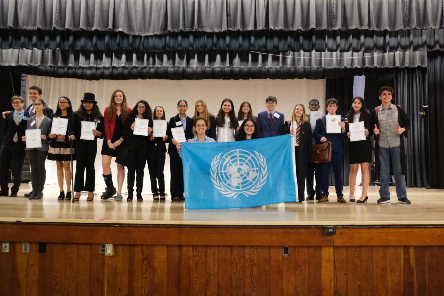 The middle school award winning delegates stand onstage with their chairs.