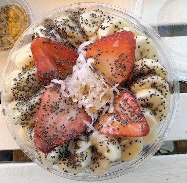 The açaí or pitaya bowl is topped with strawberries, bananas, honey, chia seeds and shredded coconut to top it off with granola on the side.