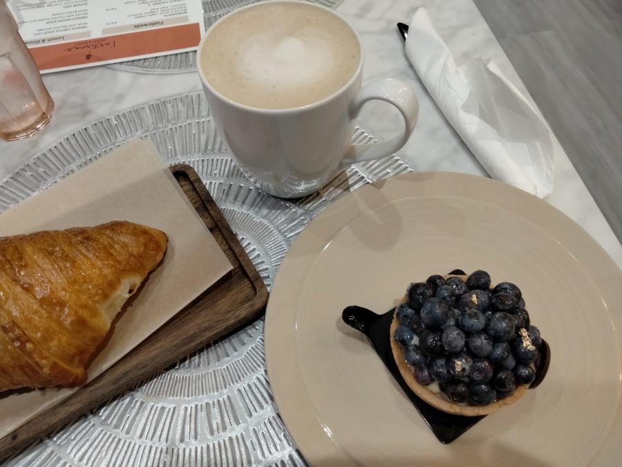 Some menu options featured at the bakery are a plain croissant with a side oat milk and a blueberry tart with a small tray to pick it up while eating.