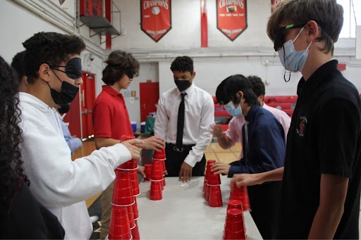 Four teams of two attempt to stack their cups into a tower while blindfolded, racing against the clock to see who finishes first.