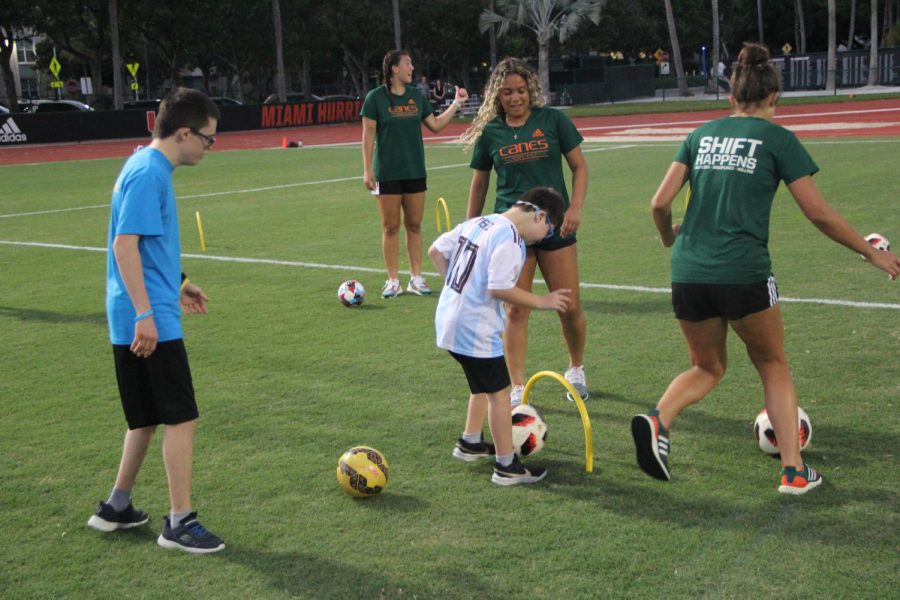 Under the guidance of UMs womens soccer team, many helped participants in kicking a ball.
