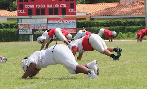 Sweating on the field, Cavalier football players stretch their calves before moving on to more drills. 