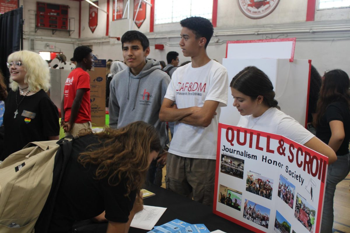 Among+numerous+other+booths+and+students%2C+sophomore+Adrian+Perez+stands+at+the+Quill+and+Scroll+booth%2C+ready+to+represent+Gables%E2%80%99+National+Journalism+Honor+Society.+