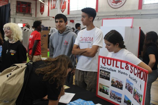 Among numerous other booths and students, sophomore Adrian Perez stands at the Quill and Scroll booth, ready to represent Gables’ National Journalism Honor Society. 
