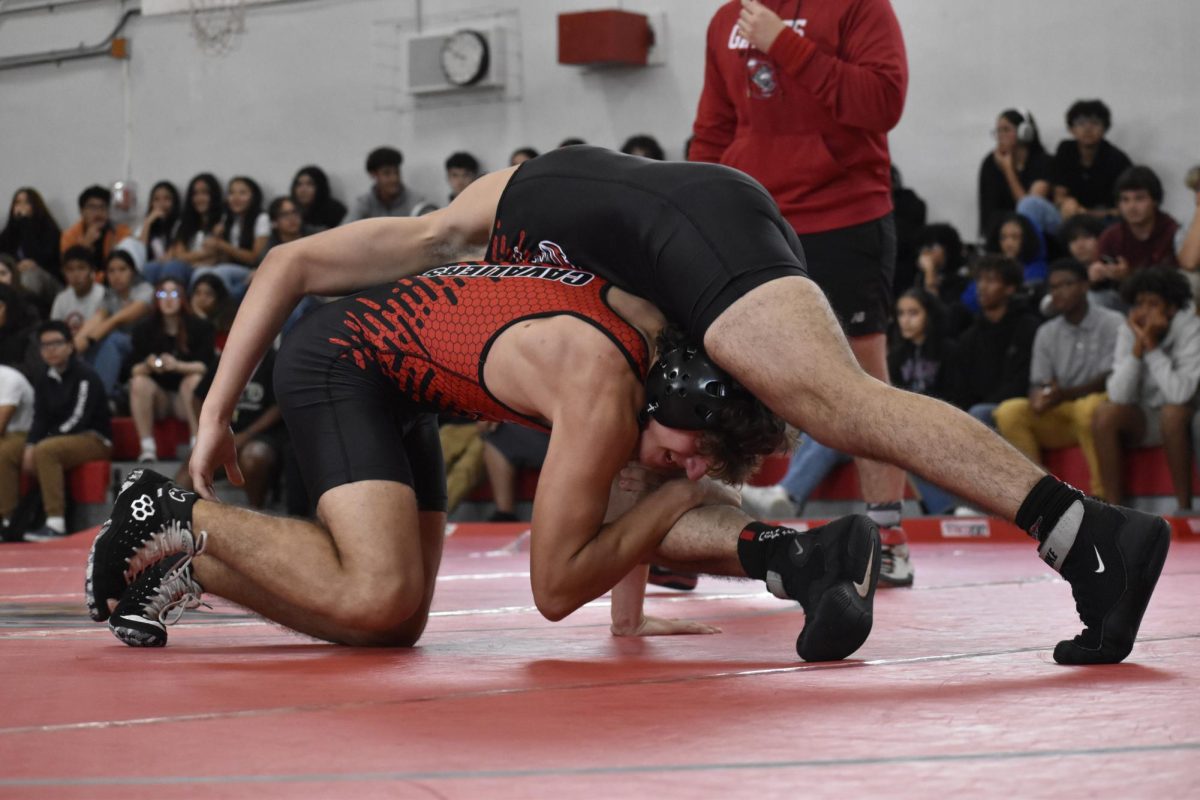 An opposing wrestler is forced to the ground as a Gables fighter sways the fight.