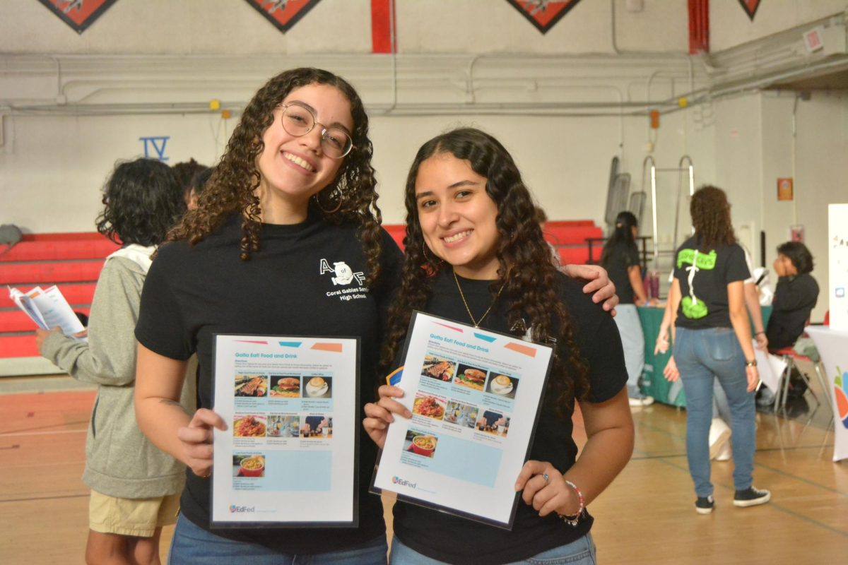 Balery Quinones and Amanda Vazquez-Gomez pose, showing off the poster that lists the values of each product sold at their booth. 