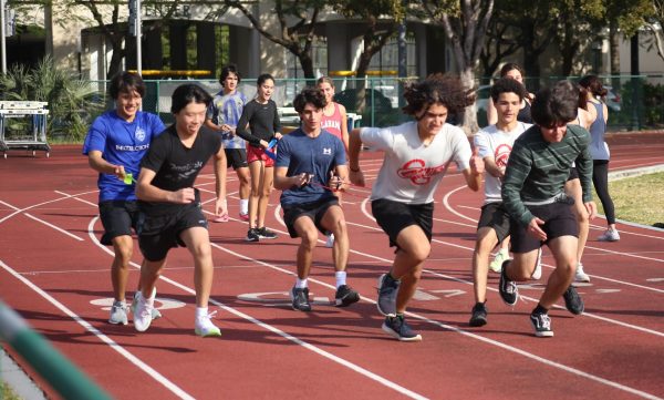 Athletes of the short-distance squad sprint down the track, fighting off the resistance bands that their partners have secured. 